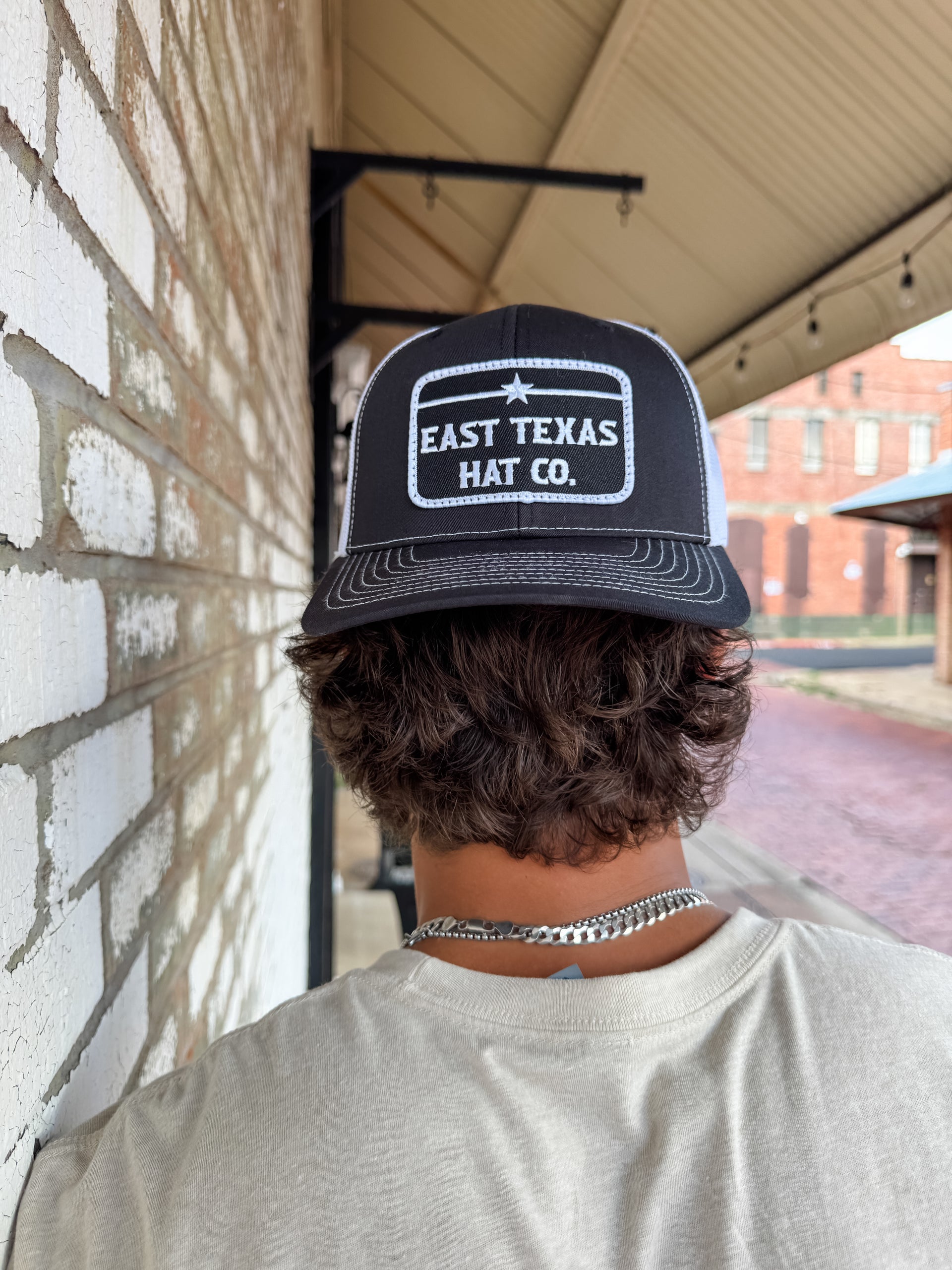 Person wearing a black and white cap with 'East Texas Hat Co.' branding against a brick wall.