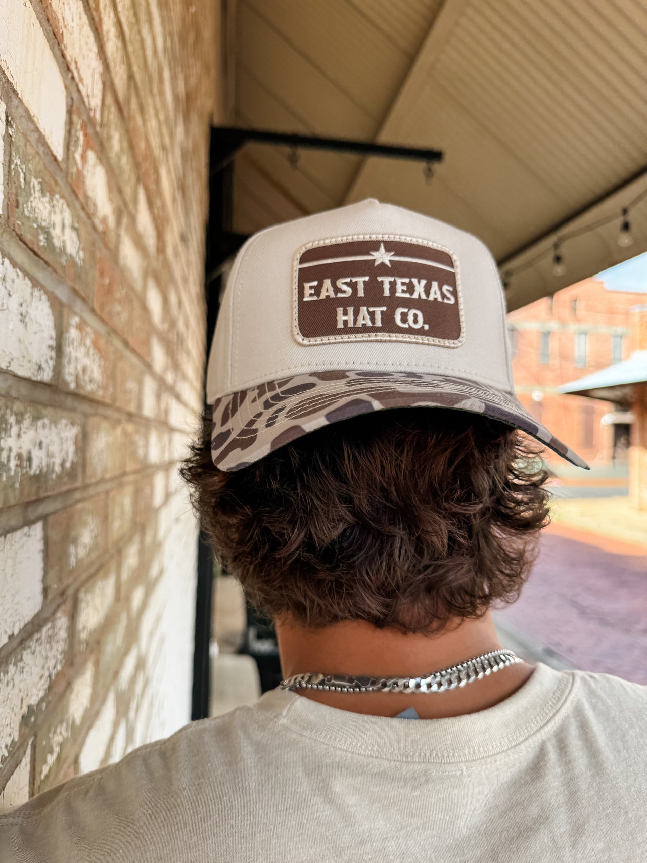 Person wearing an 'East Texas Hat Co.' cap outdoors near a brick wall.