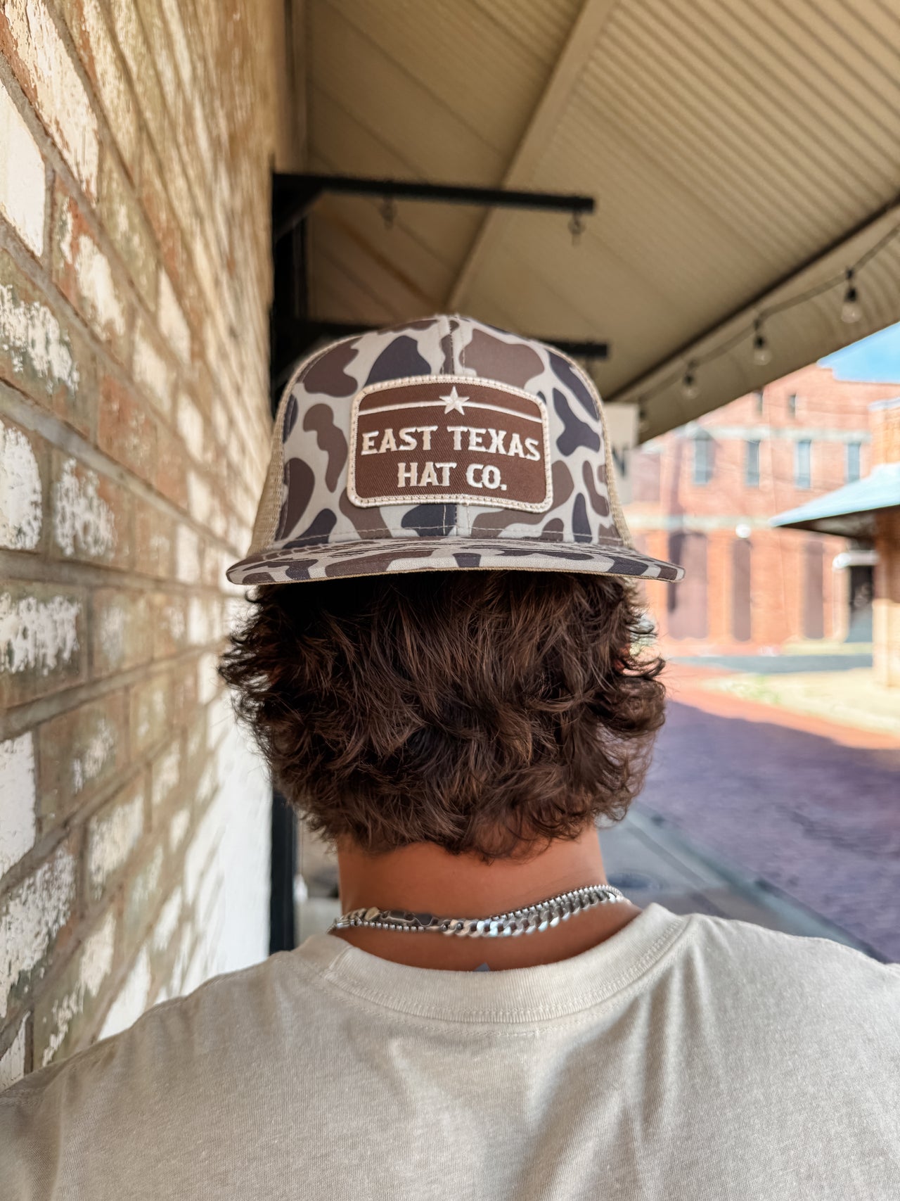 Person wearing a 'East Texas Hat Co.' cap standing in front of a brick wall.