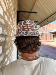 Person wearing a 'East Texas Hat Co.' cap standing in front of a brick wall.