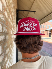 Person wearing a red 'Red Dirt Hat Co' cap in front of a brick wall.