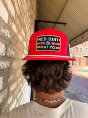 Person wearing a red 'Red Dirt Hat Co.' cap against a brick wall.