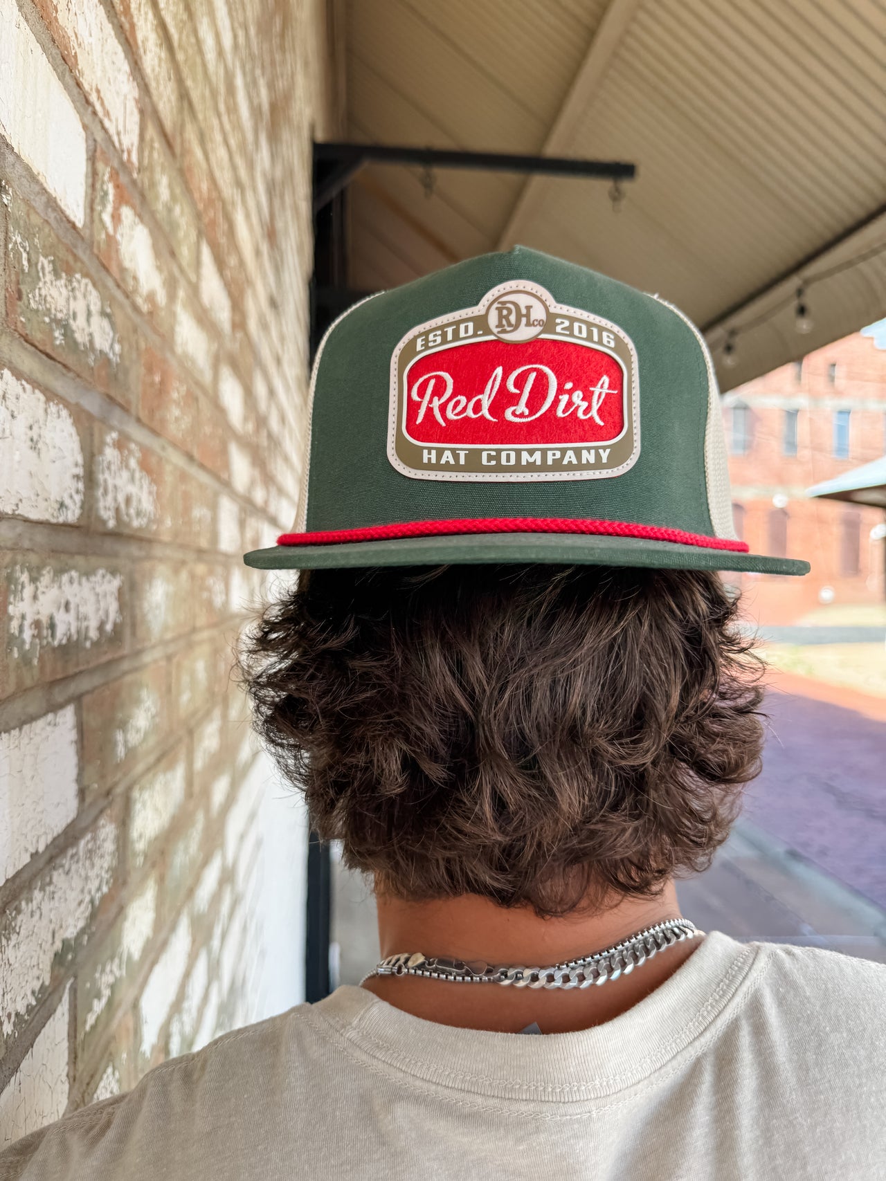 Person wearing a 'Red Dirt Hat Company' cap with a brick wall and window in the background