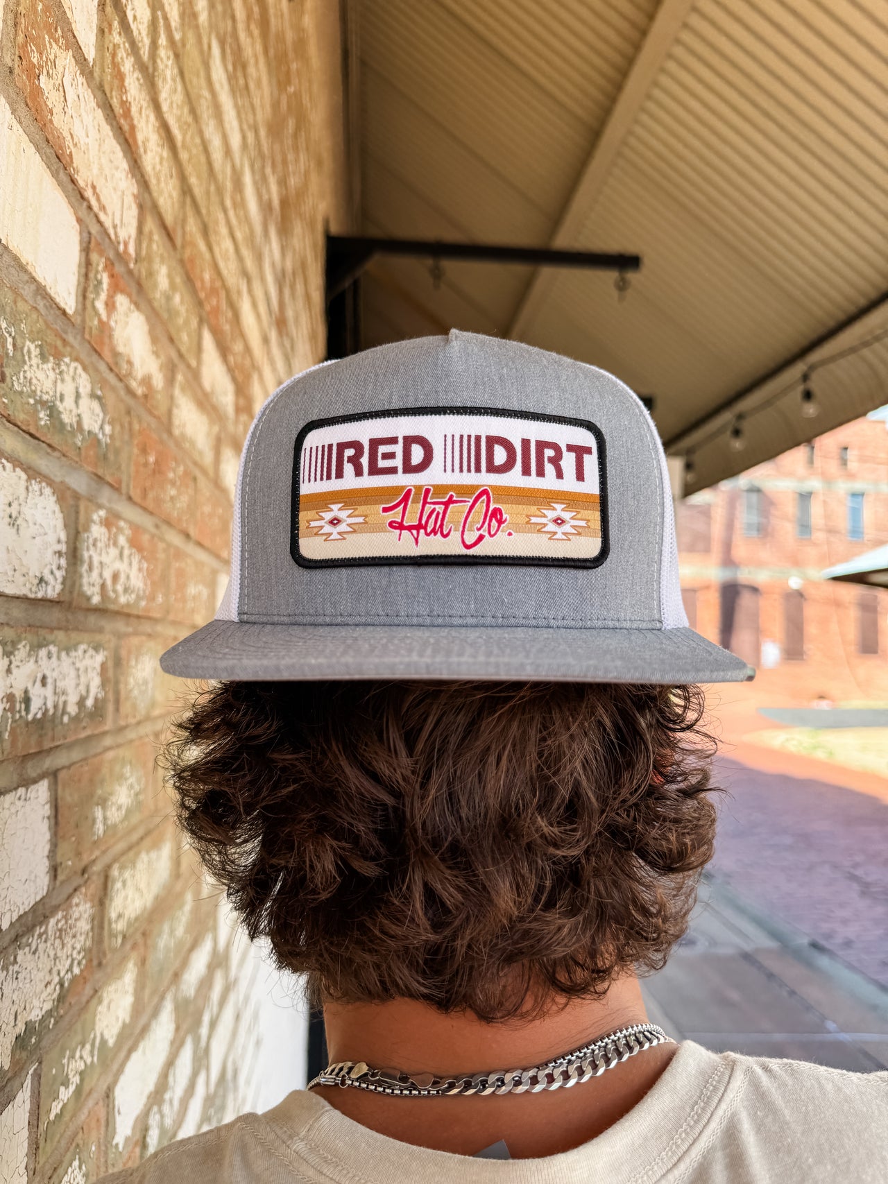 Person wearing a gray cap with 'Red Dirt Hat Co' logo against a brick wall.