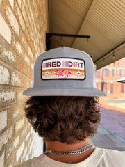 Person wearing a gray cap with 'Red Dirt Hat Co' logo against a brick wall.