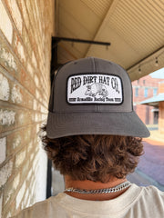 Person wearing a gray cap with 'Red Dirt Hat Co.' logo, standing against a textured wall.