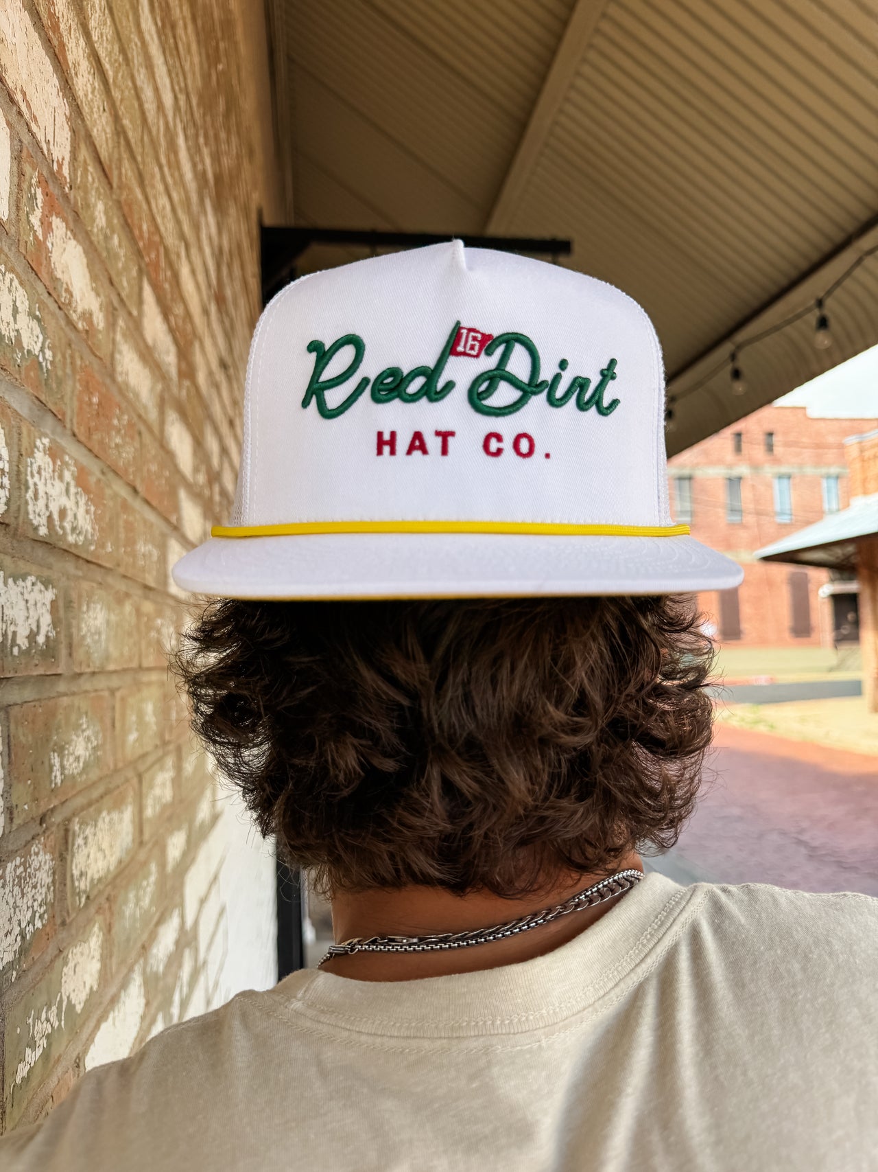 Person wearing a white cap with 'Red Dirt Hat Co.' logo, standing in front of a brick wall.