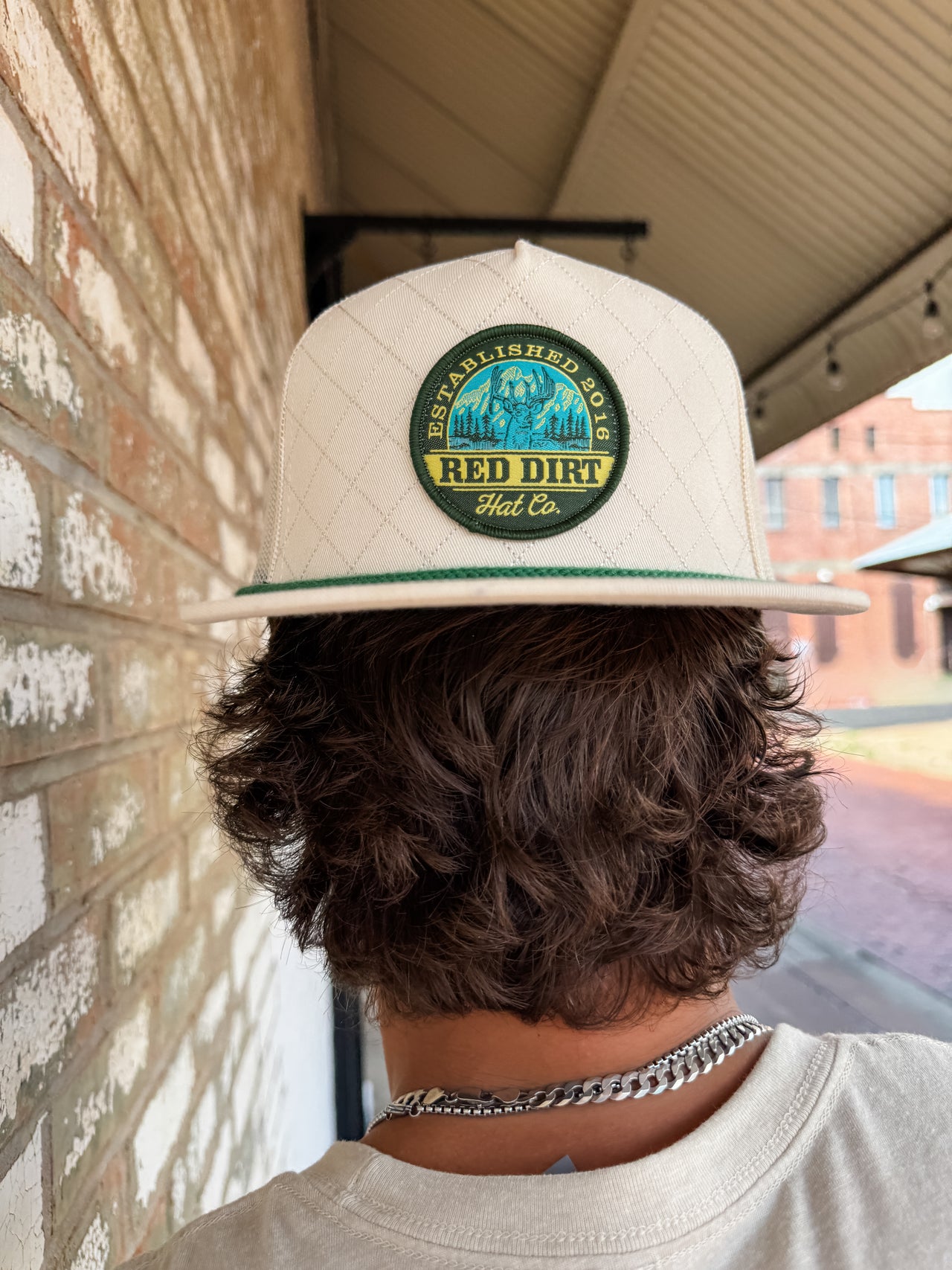Person wearing a beige cap with a 'Red Dirt Hat Co.' logo, standing against a brick wall.