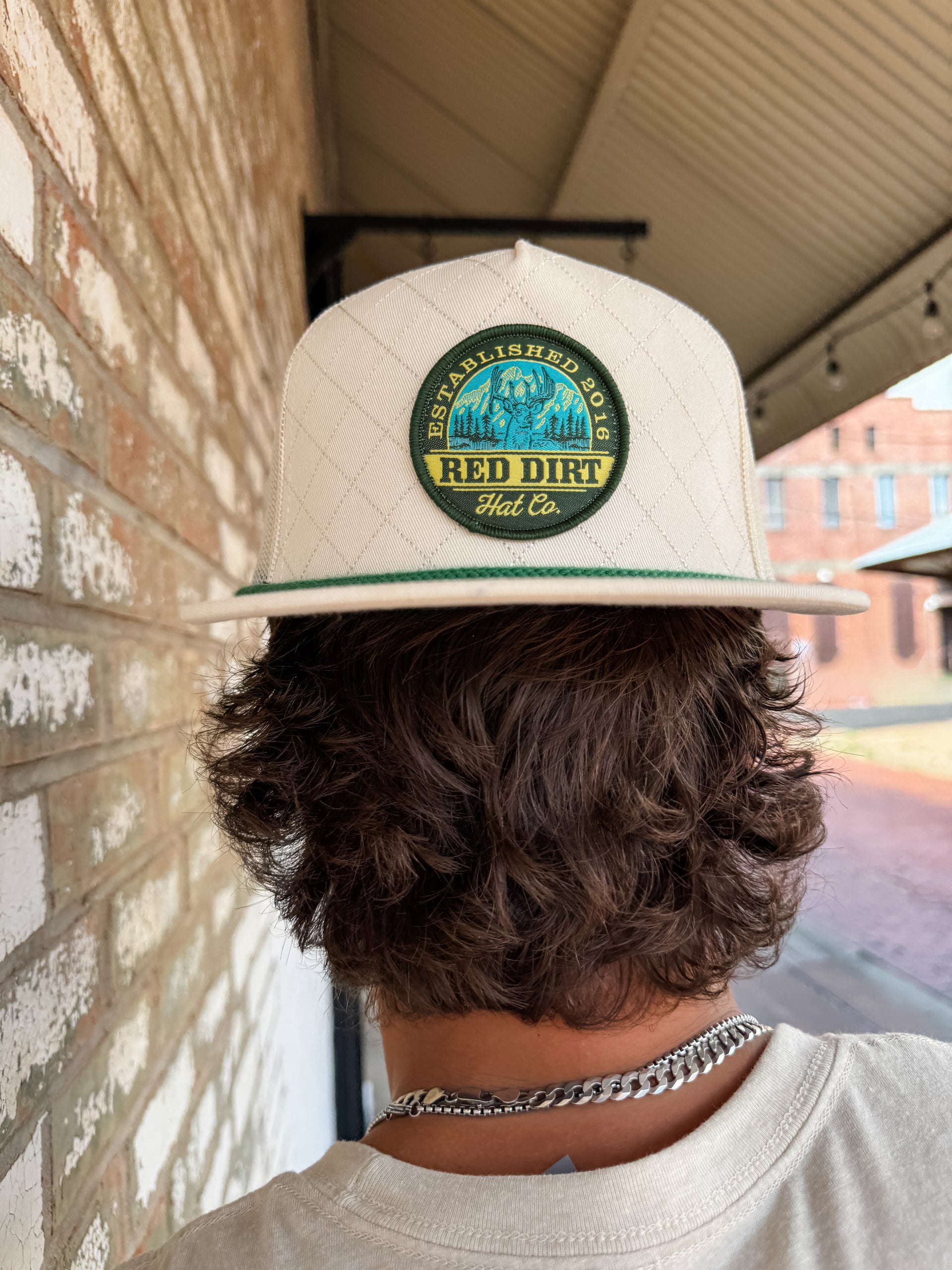 Person wearing a beige cap with a 'Red Dirt Hat Co.' logo, standing against a brick wall.