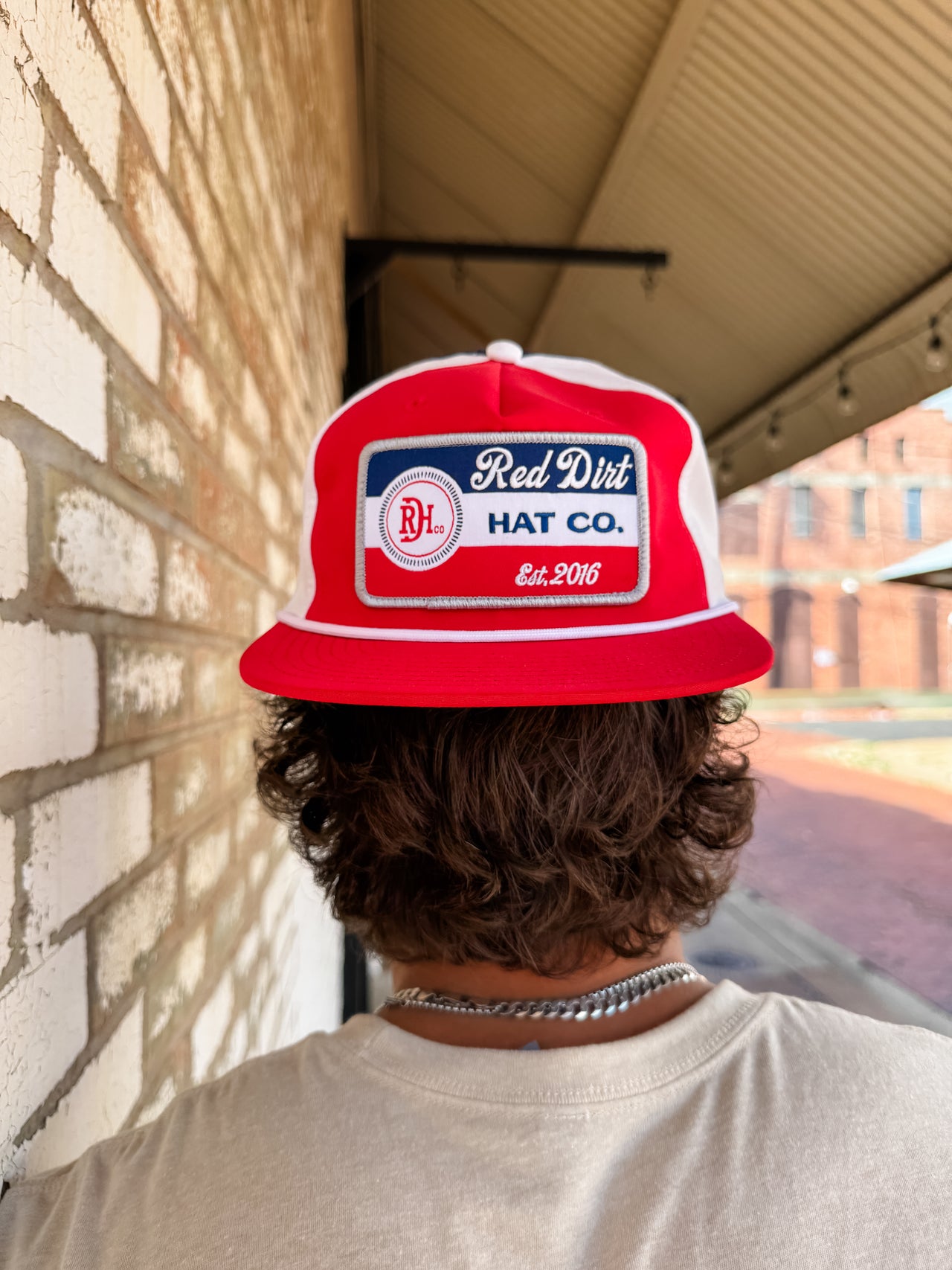 Person wearing a red and white cap with 'Red Dirt Hat Co.' logo against a brick wall.