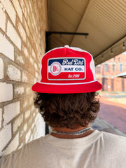 Person wearing a red and white cap with 'Red Dirt Hat Co.' logo against a brick wall.