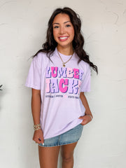 Woman wearing a light purple t-shirt with colorful text, standing against a white wall.