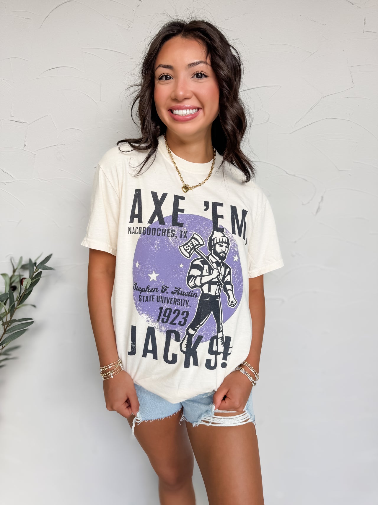 Woman wearing a white t-shirt with graphic design and text, standing against a light gray wall.