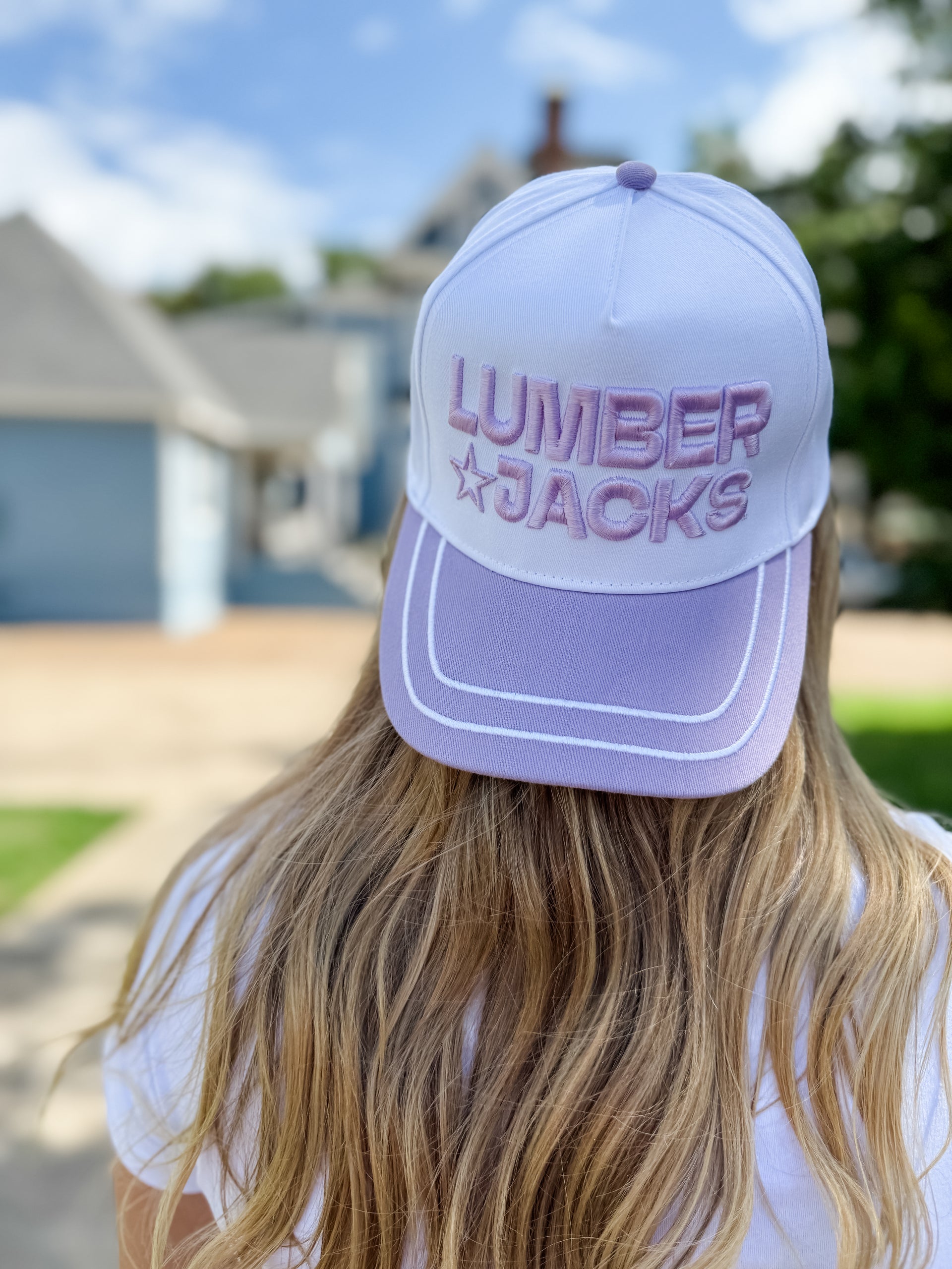 Person wearing a 'LUMBER JACKS' cap outdoors with a house in the background