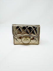 A small, compact metallic gold wallet with a high-gloss finish displayed against a solid white background. The wallet features a diamond-quilted pattern, a curved front flap, and a polished gold-toned metal turn-lock closure.