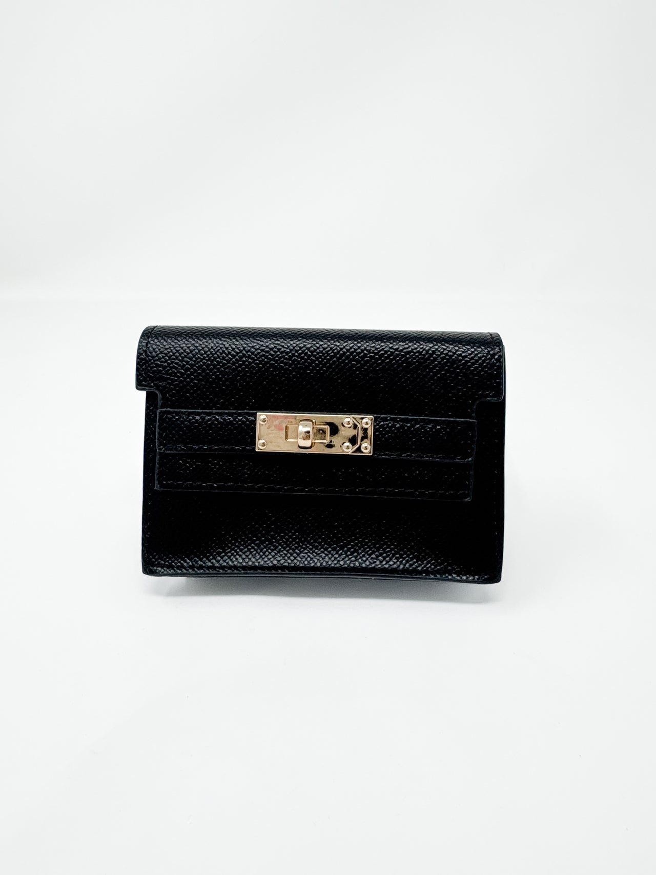 A small, structured black faux-leather wallet shown against a plain white background. The wallet features a fine textured, pebbled finish, a classic front flap design, and a polished gold rectangular turn-lock closure.