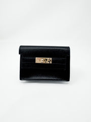 A small, structured black faux-leather wallet shown against a plain white background. The wallet features a fine textured, pebbled finish, a classic front flap design, and a polished gold rectangular turn-lock closure.