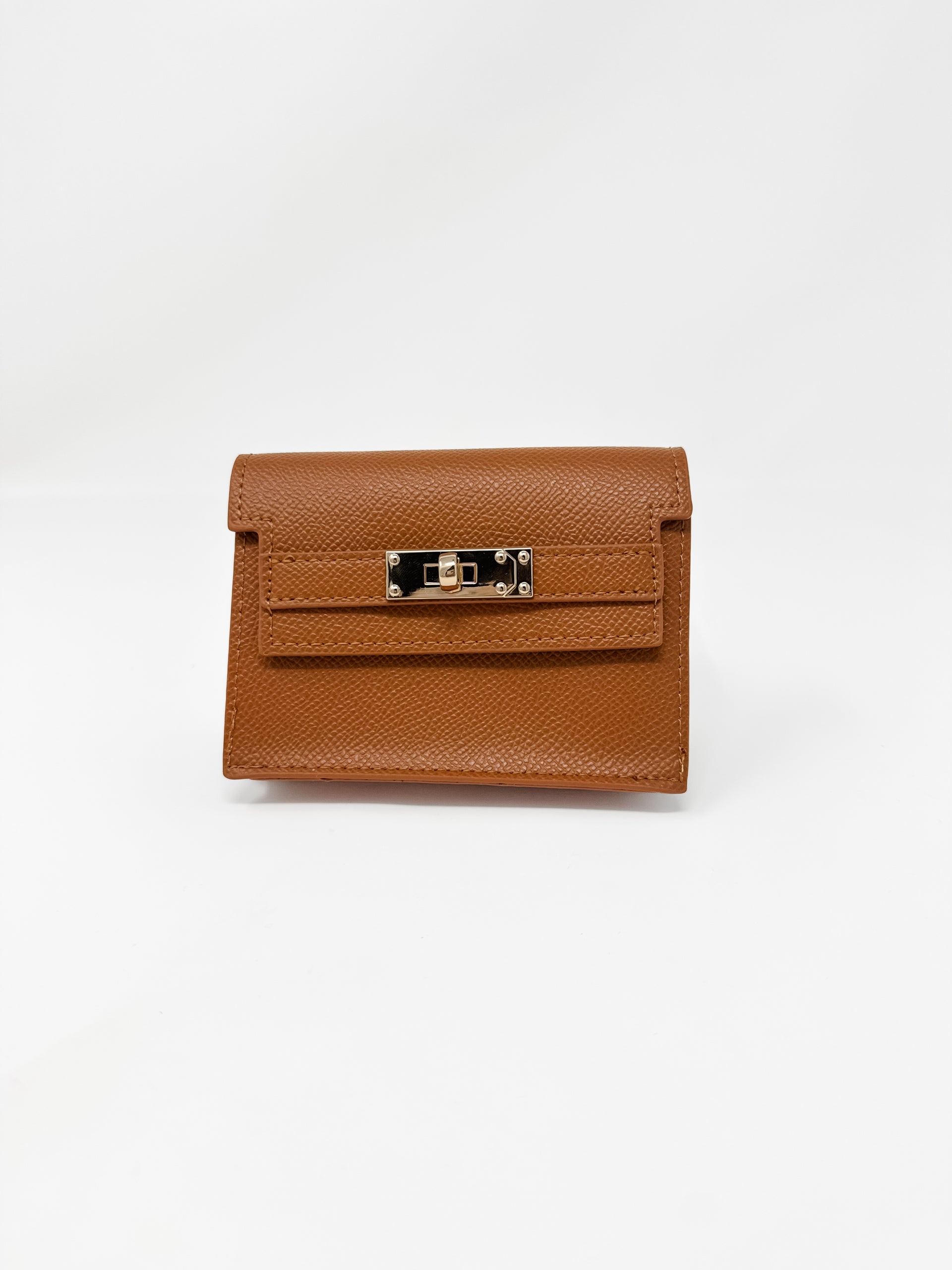 A small, structured camel-brown faux-leather wallet shown against a plain white background. The wallet features a fine textured, pebbled finish, a classic front flap design, and a polished gold rectangular turn-lock closure.