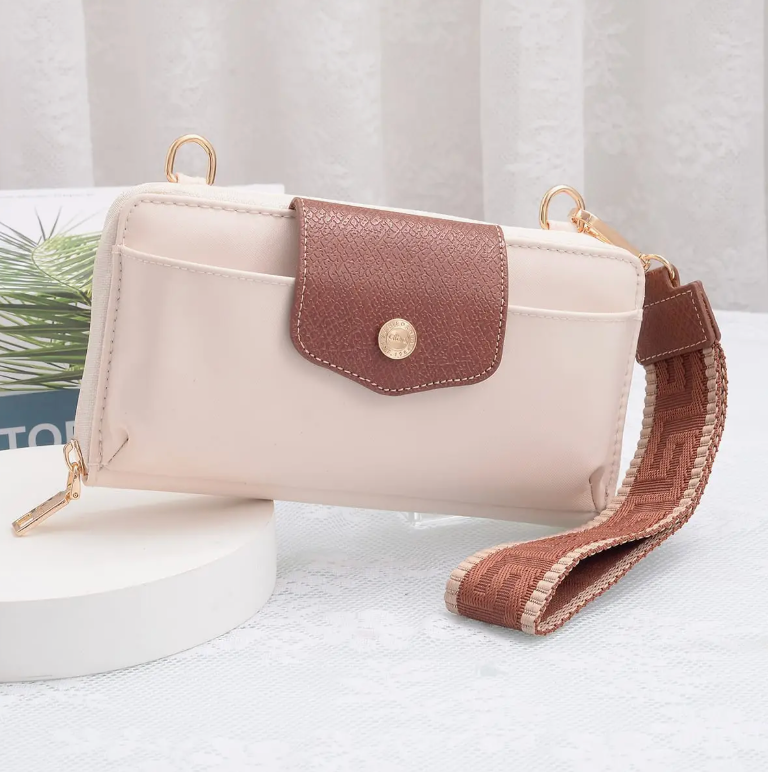 A small rectangular crossbody bag in pale blush pink faux leather with a brown textured flap pocket, gold-tone hardware, and a matching brown woven shoulder strap, displayed on a white pedestal against a soft light gray background.