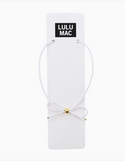 A white beaded bracelet with a small gold bead accent, displayed on a white card labeled 'LULU MAC' against a white background.