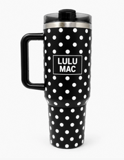 A black travel tumbler with white polka dots and a black handle, featuring a central white square label that reads 'LULU MAC' in bold white text. The tumbler has a stainless steel band near the lid and a black lid with a clear rim, shown on a light gray background.