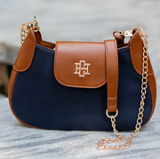 A navy blue and brown leather shoulder bag with a gold-tone cross logo on the front flap and a gold chain strap, resting on a gray marble surface.