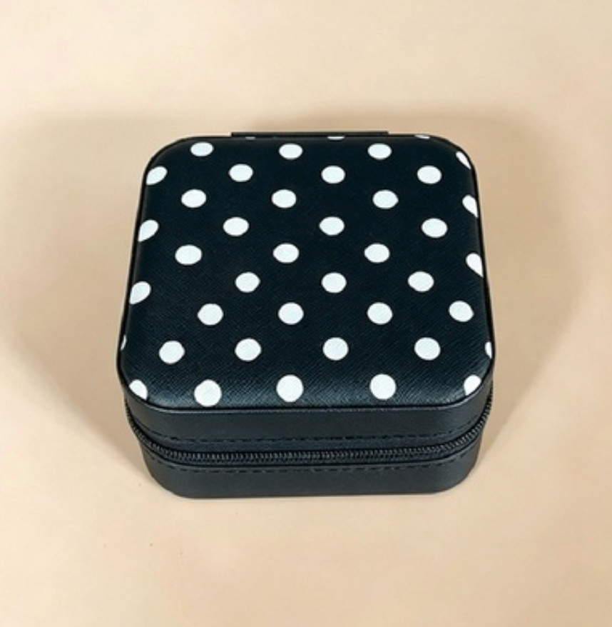 A small square zippered case with a black body and a black lid covered in white polka dots, photographed on a plain beige background.