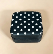 A small square zippered case with a black body and a black lid covered in white polka dots, photographed on a plain beige background.