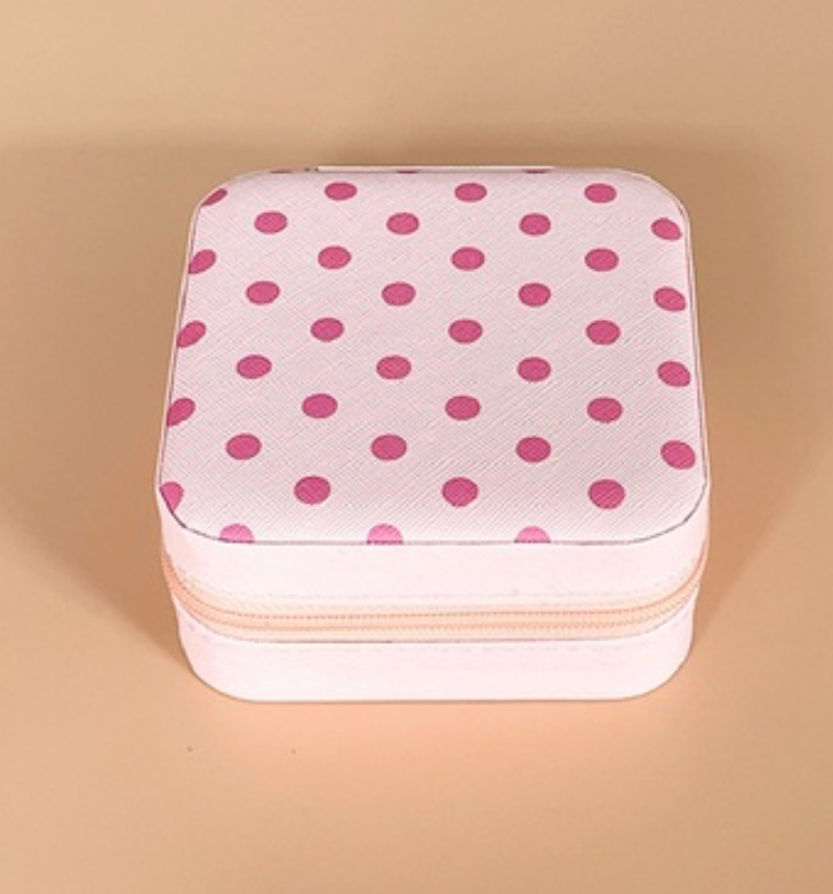 A square white zippered case with a pink polka dot pattern on the lid, set against a solid beige background.
