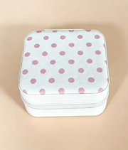 A square zippered storage case with a white textured surface covered in pink polka dots, set against a solid beige background.