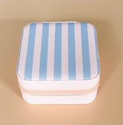 A square zippered storage case with a light pink  and light blue vertically striped pattern on the lid, shown on a solid beige background.