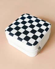 A square zippered case with a black and white checkerboard pattern on the top, shown on a solid peach background.