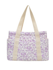 A fabric tote bag with a light purple floral print on a white background, featuring two thick beige shoulder straps and a front pocket.