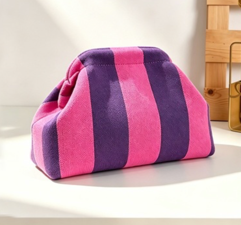 A small drawstring pouch bag with vertical pink and purple stripes, resting on a white surface with a wooden box in the background.