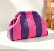 A small drawstring pouch bag with vertical pink and purple stripes, resting on a white surface with a wooden box in the background.
