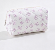 A quilted cosmetic pouch with a white background and a repeating pattern of light purple bow outlines, featuring a silver zipper pull on the left side.