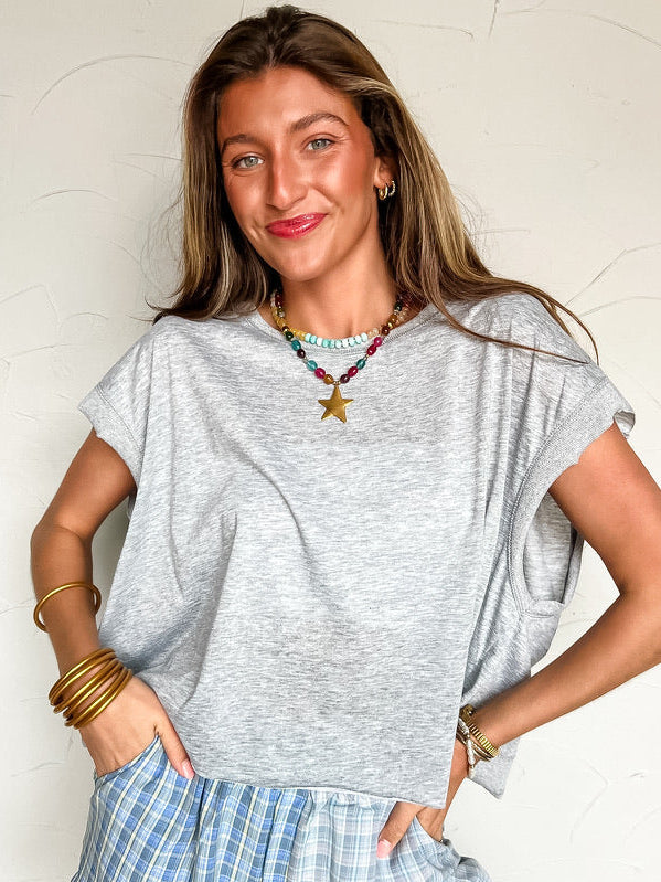 a girl wearing a grey top with blue plaid shorts against a white wall