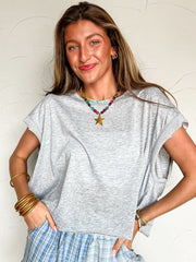 a girl wearing a grey top with blue plaid shorts against a white wall