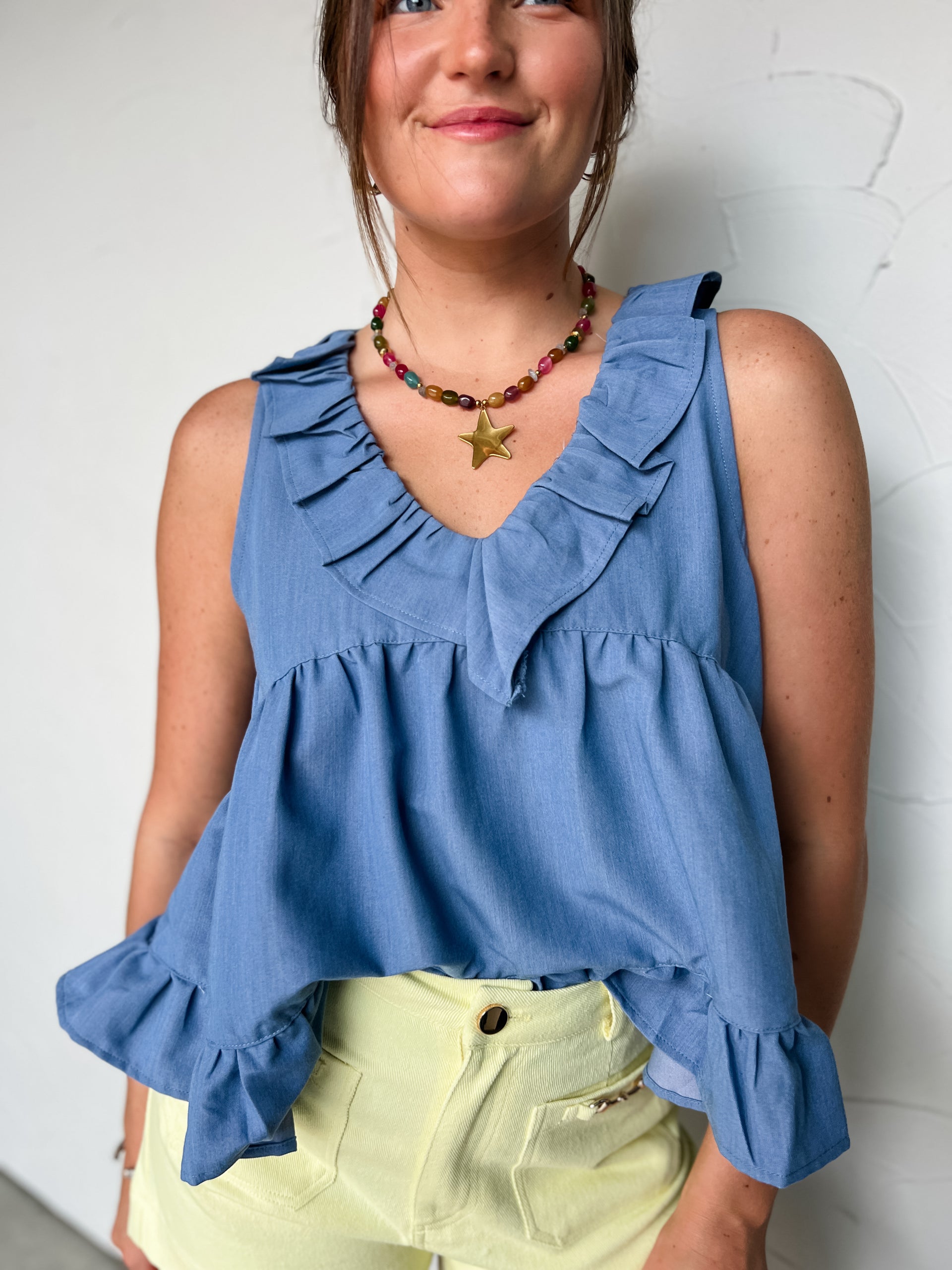 Woman wearing a blue sleeveless top with ruffles against a white background