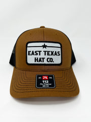 Brown and black trucker hat with mesh back and “East Texas Hat Co.” patch on the front.