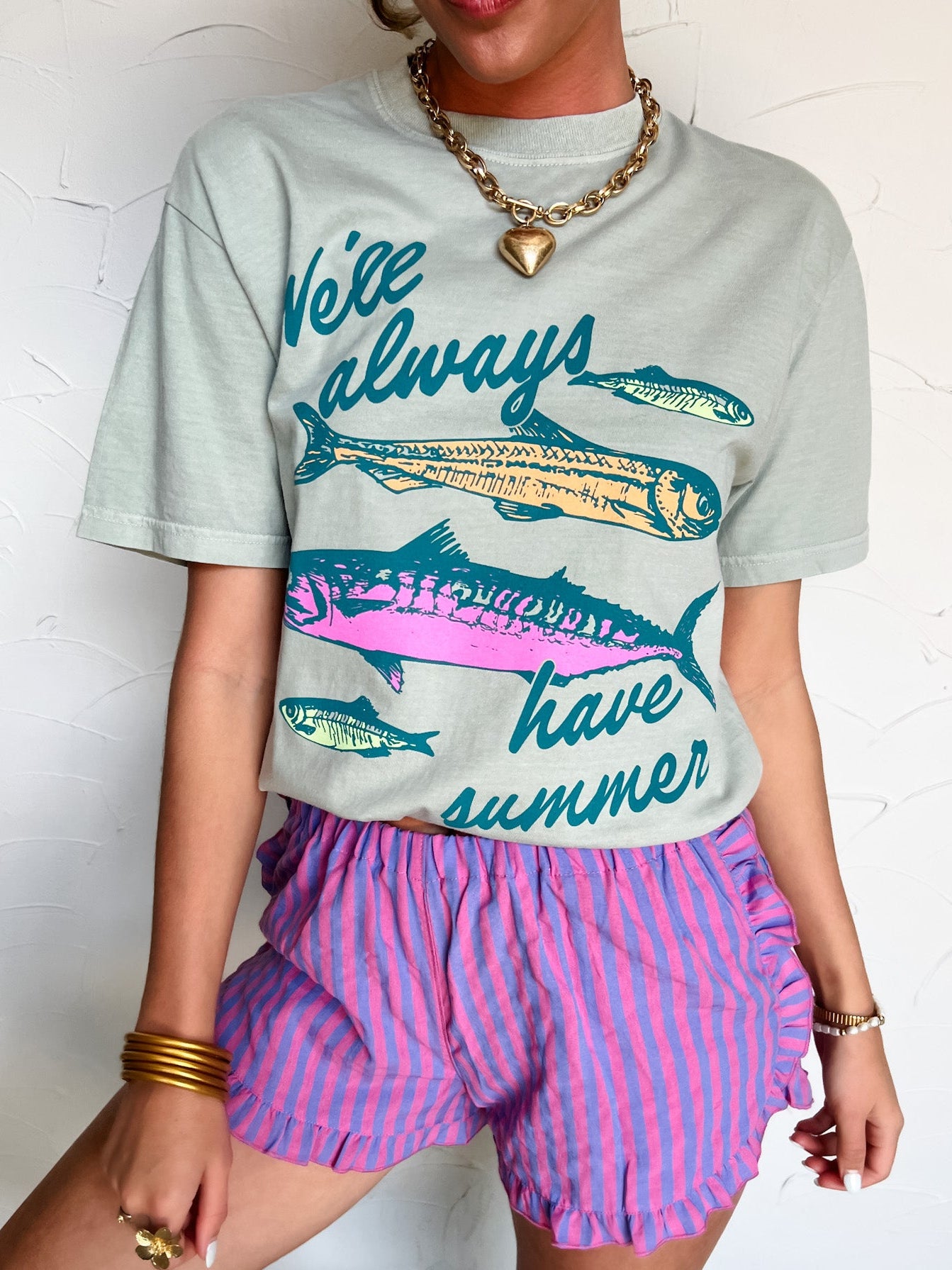 Person wearing a graphic t-shirt with fish design and text, paired with pink striped shorts on a white background.