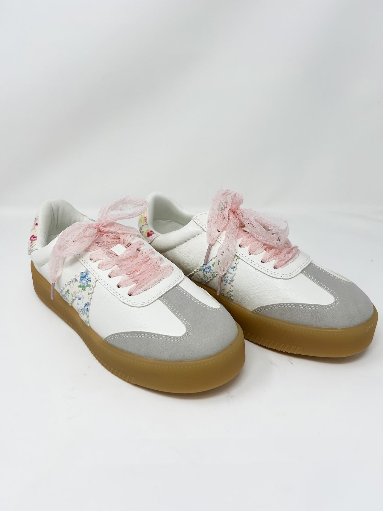 Pair of sneakers with floral lace and light gray detail on a white background