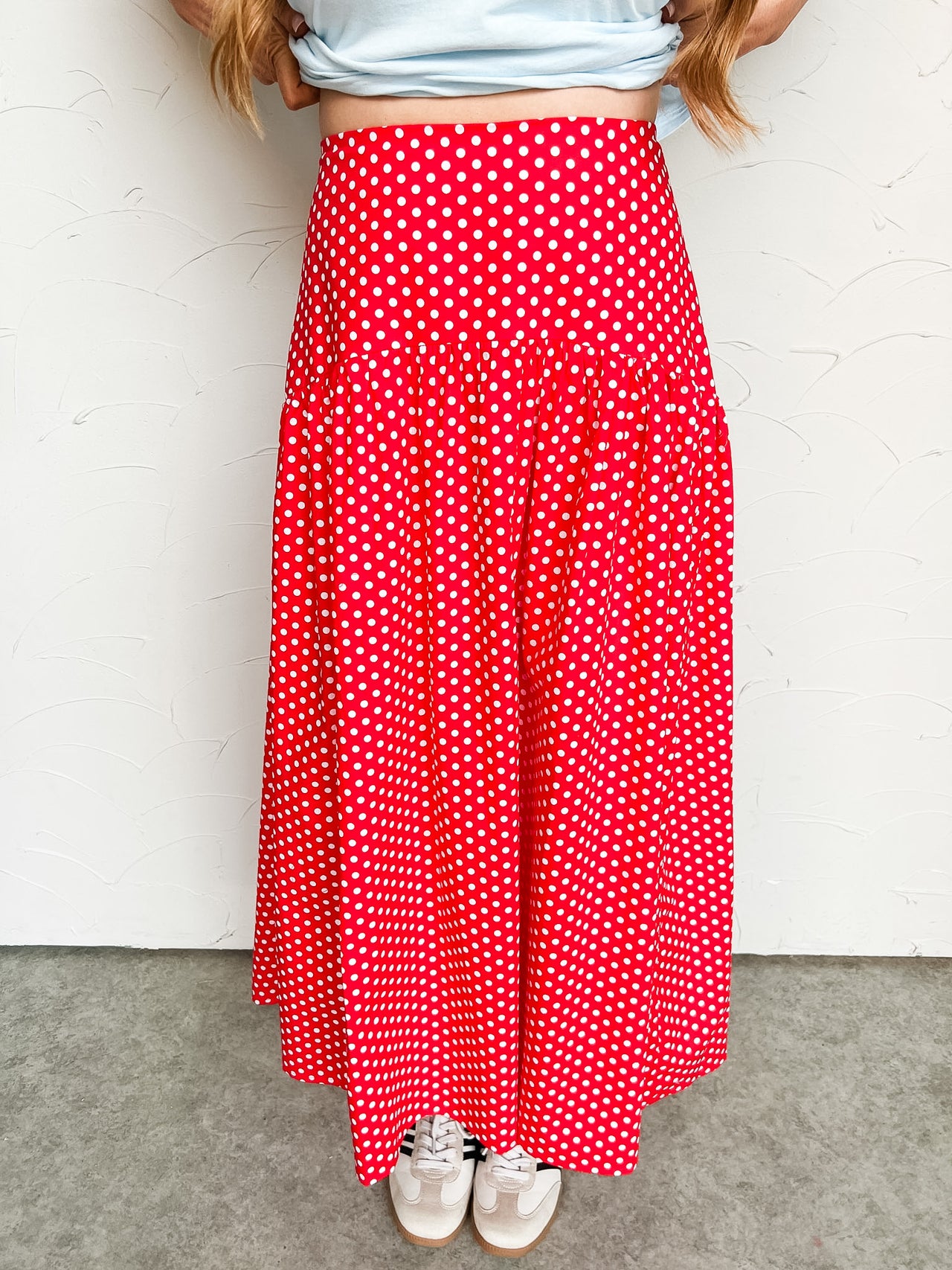 Person wearing a red midi polka dot skirt against a white wall.