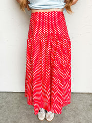 Person wearing a red midi polka dot skirt against a white wall.