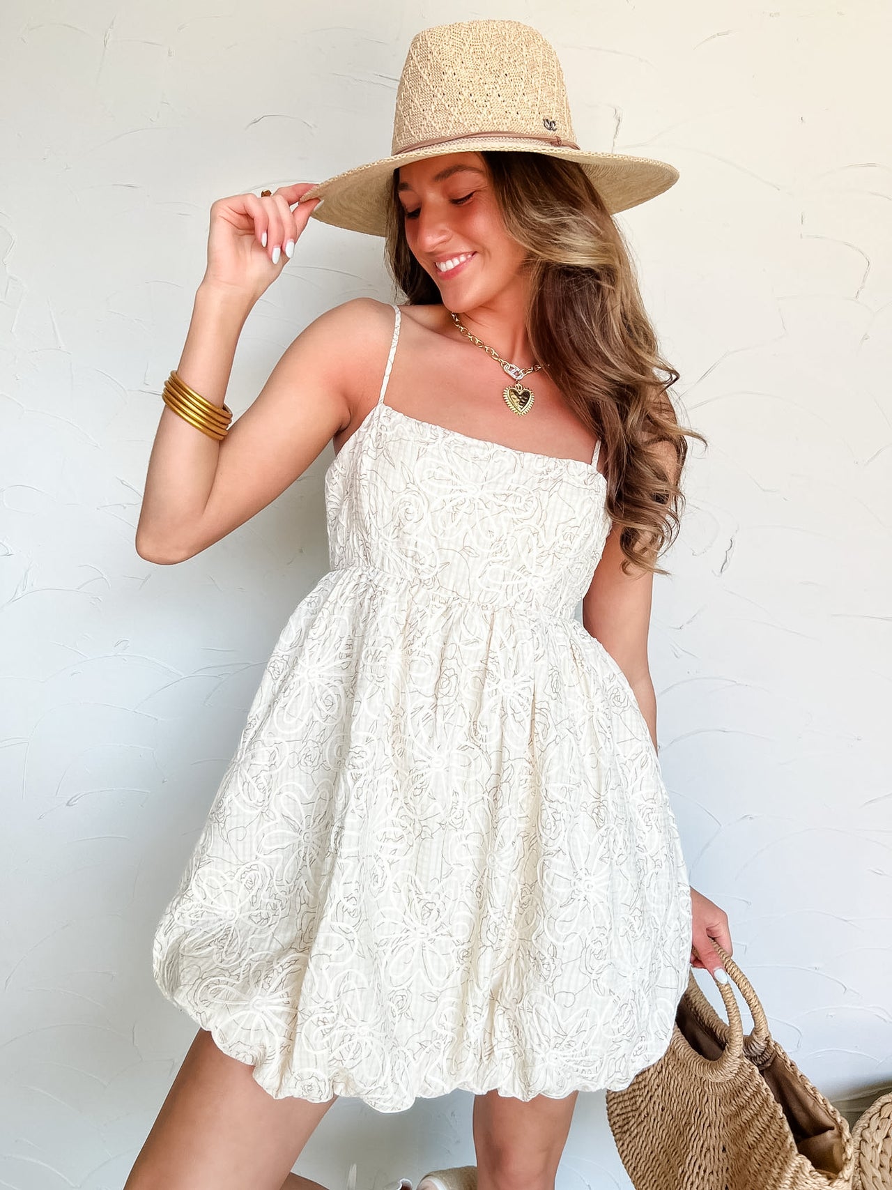 Woman wearing a white lace dress and straw hat against a light background