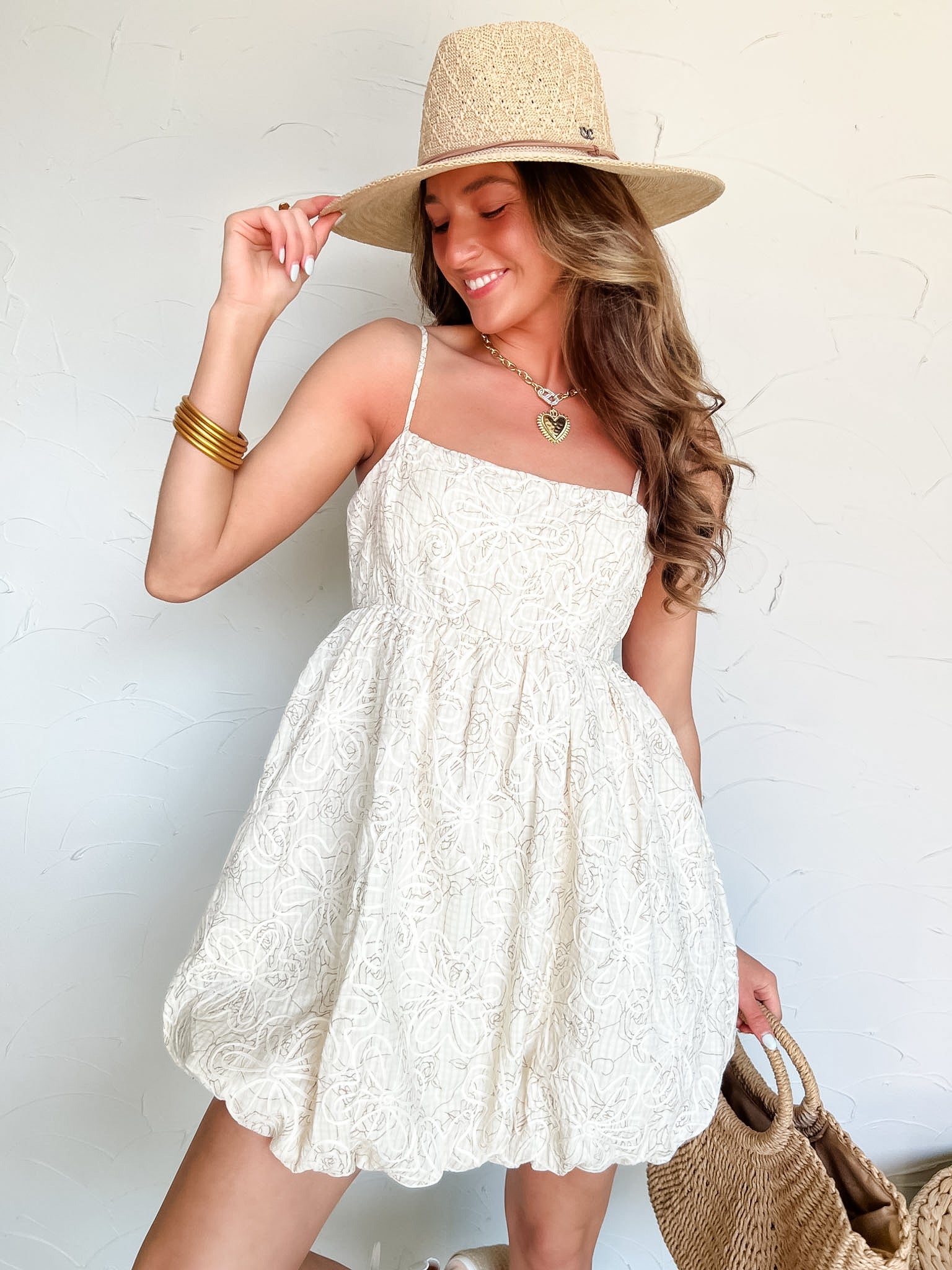 Woman wearing a white lace dress and straw hat against a light background