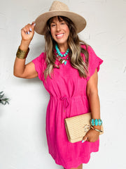 Woman wearing a pink dress, straw hat, and turquoise jewelry against a white background