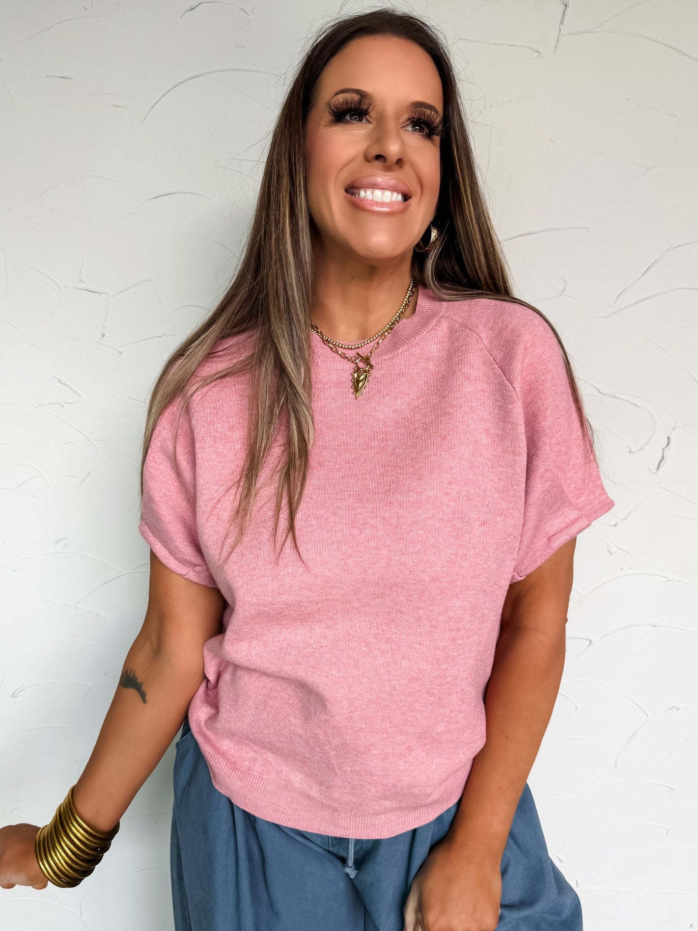 Woman wearing a pink t-shirt and blue pants against a white wall
