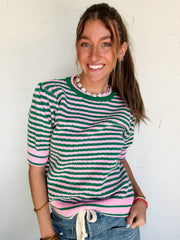 Woman wearing a green and pink striped sweater against a white wall
