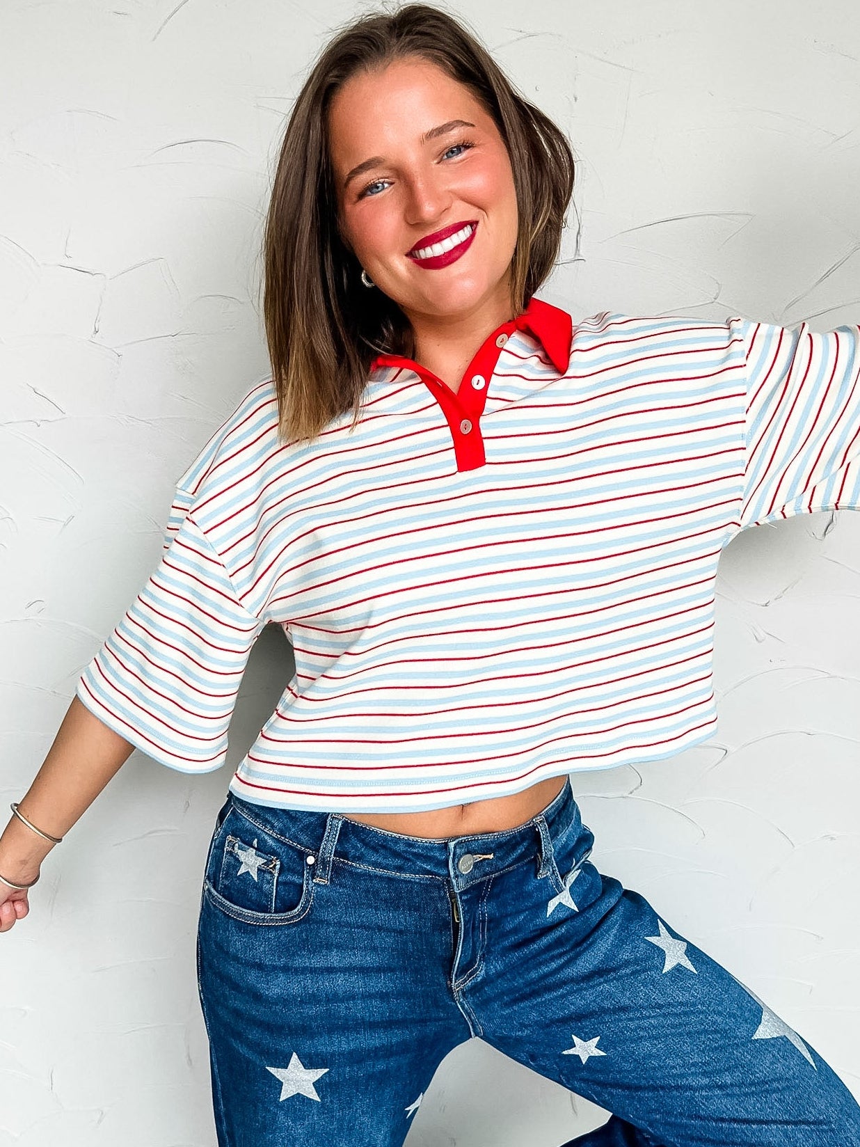 Woman wearing a red and white striped shirt with a red collar and blue jeans with star patterns against a white background.